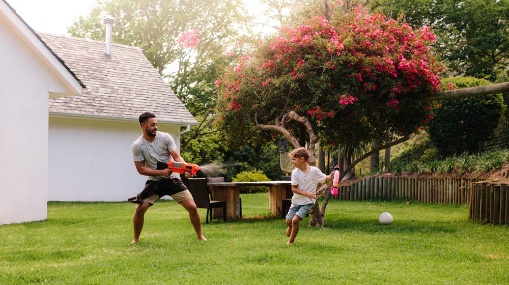 father and son having a water gun fight in the backyard